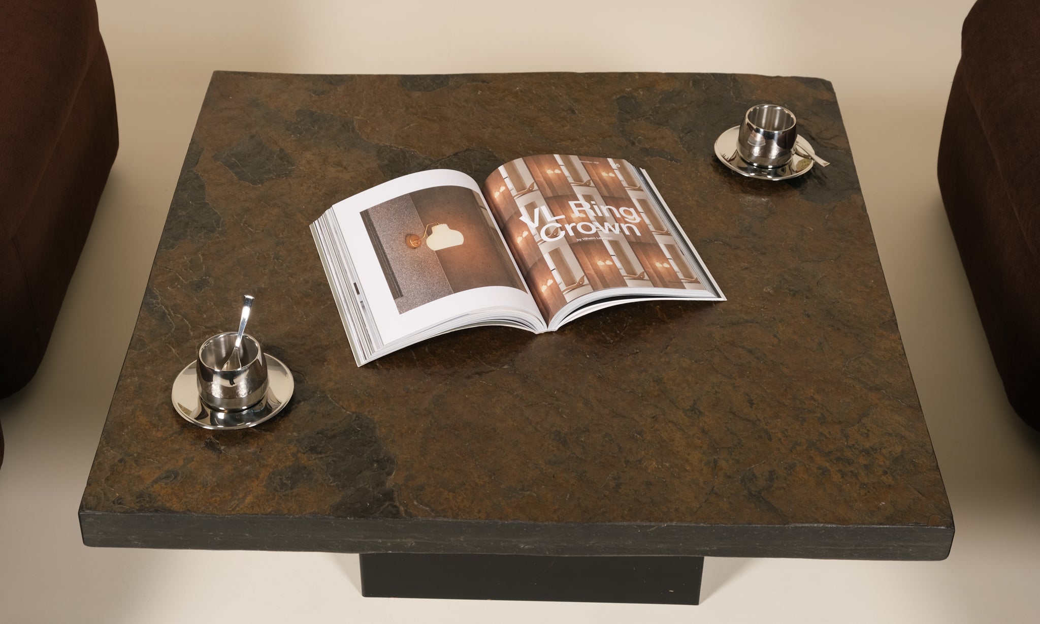 Open magazine on a dark stone coffee table with two silver espresso cups