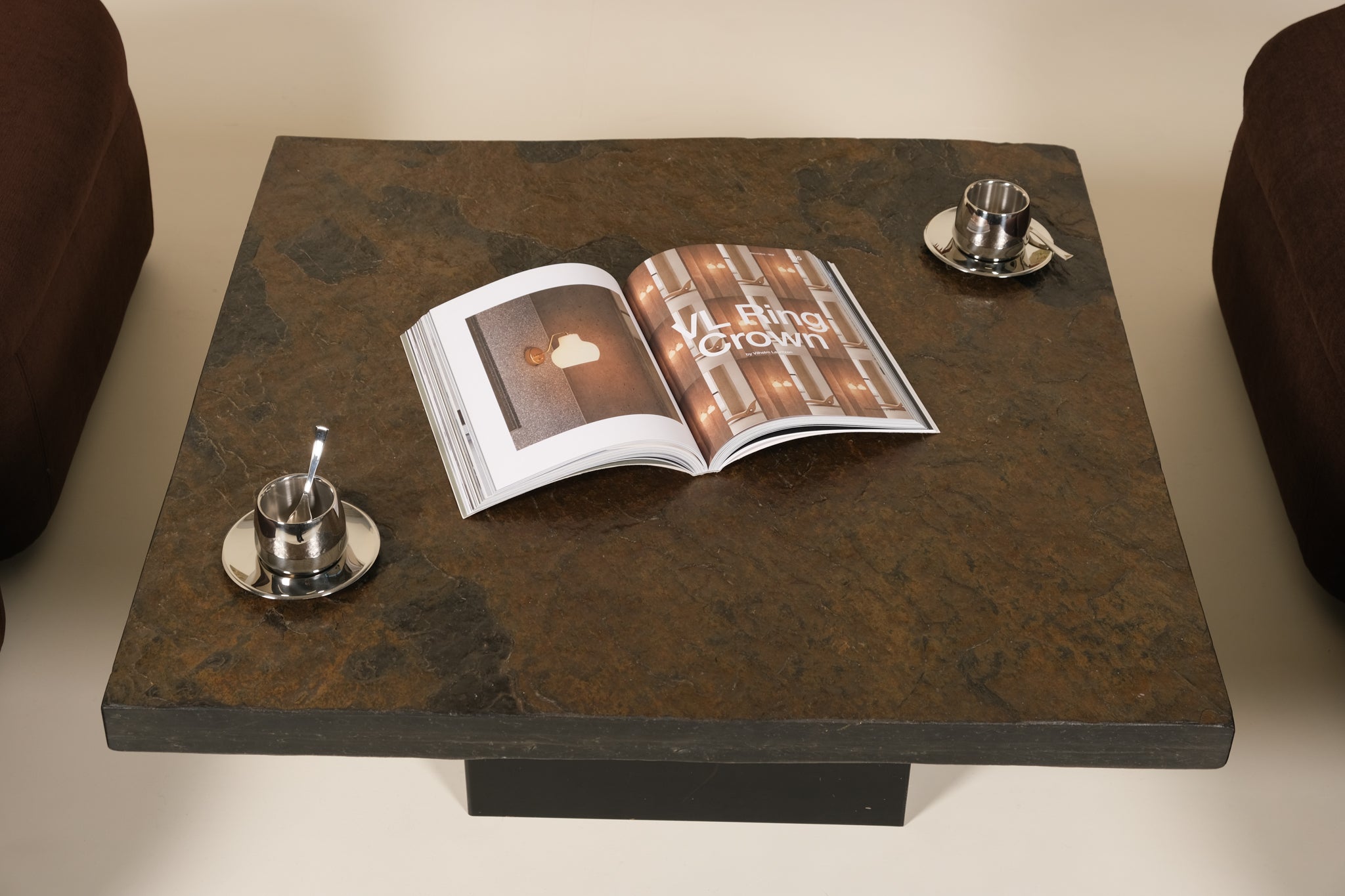 Open magazine on a dark stone coffee table with two silver espresso cups