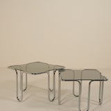 Two glass tables with chrome frames on a beige background