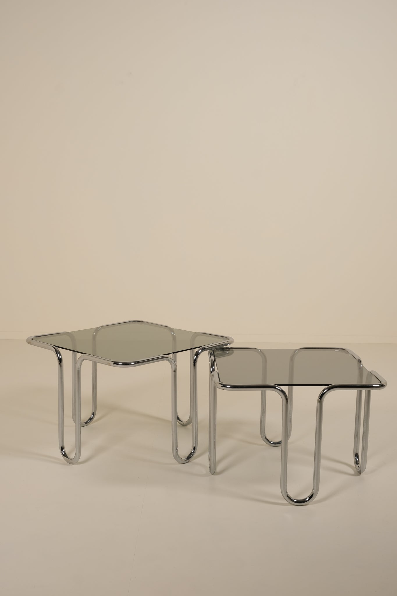 Two glass tables with chrome frames on a beige background