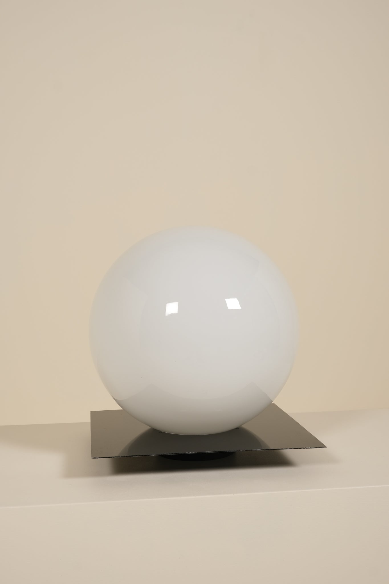 White spherical lamp on a metallic stand against a beige background
