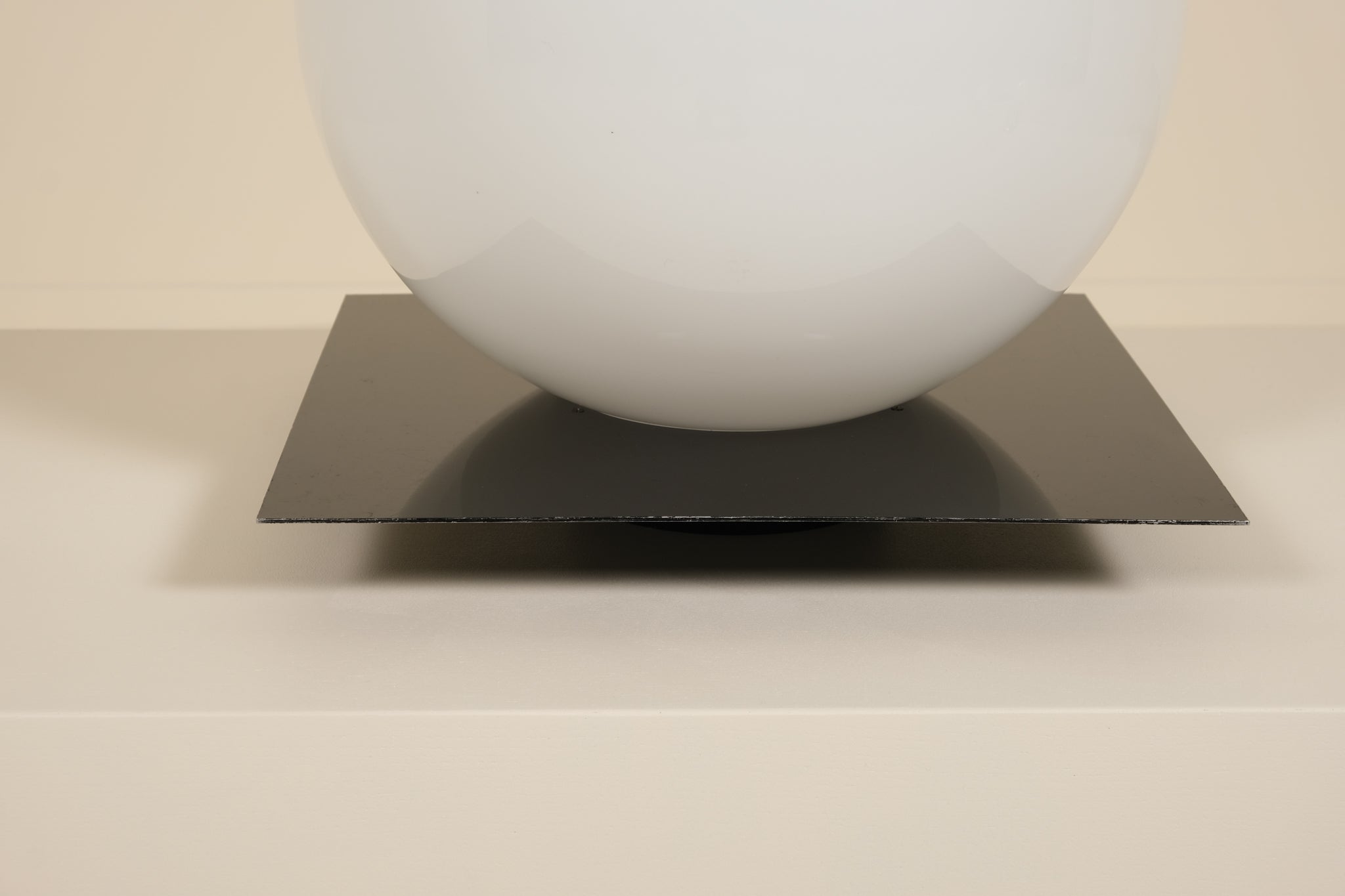 White sphere on a black square platform against a beige background
