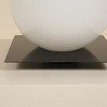 White sphere on a black square platform against a beige background