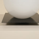 White sphere on a black square platform against a beige background