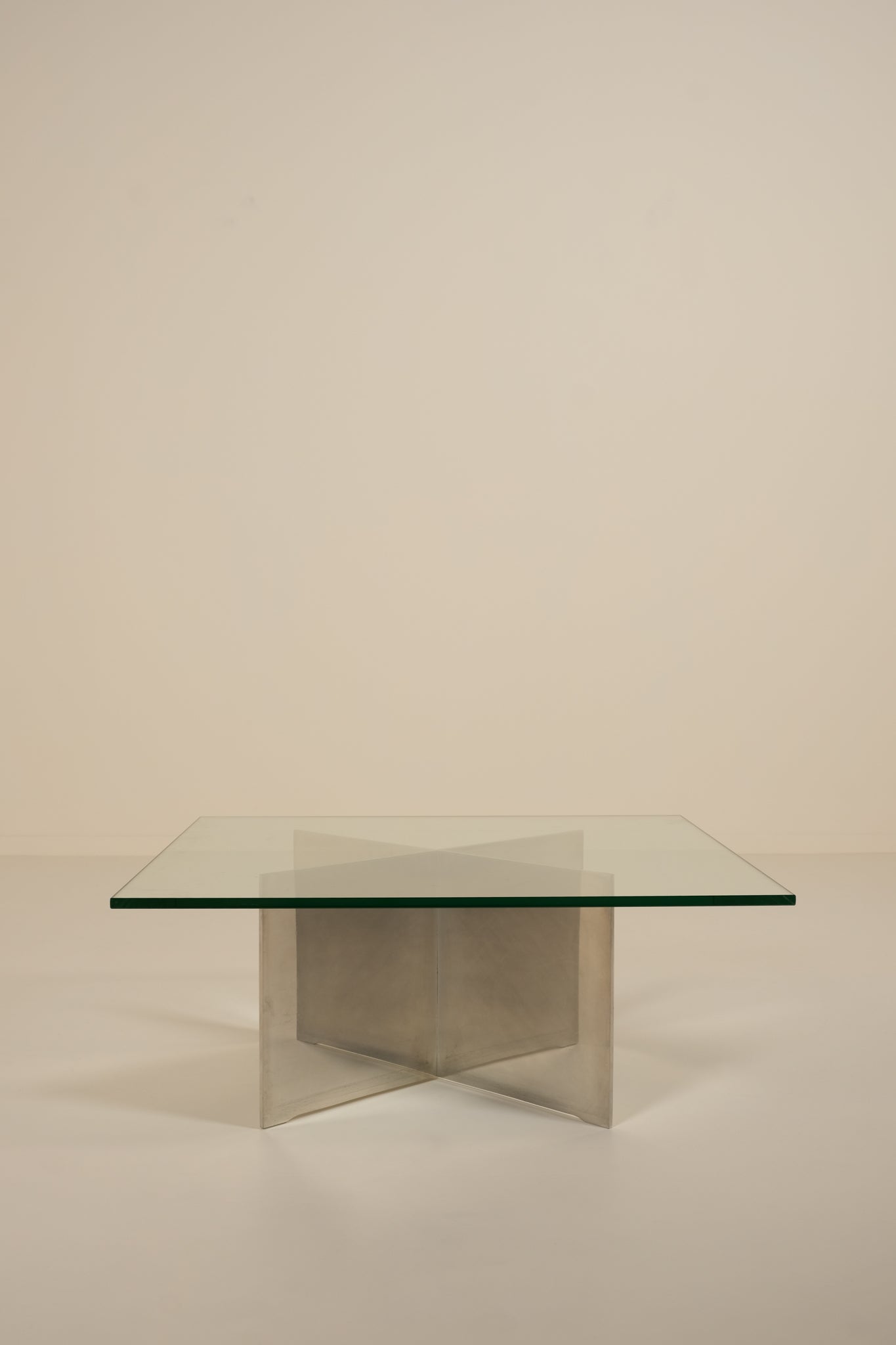 Glass table with metal base on a beige background