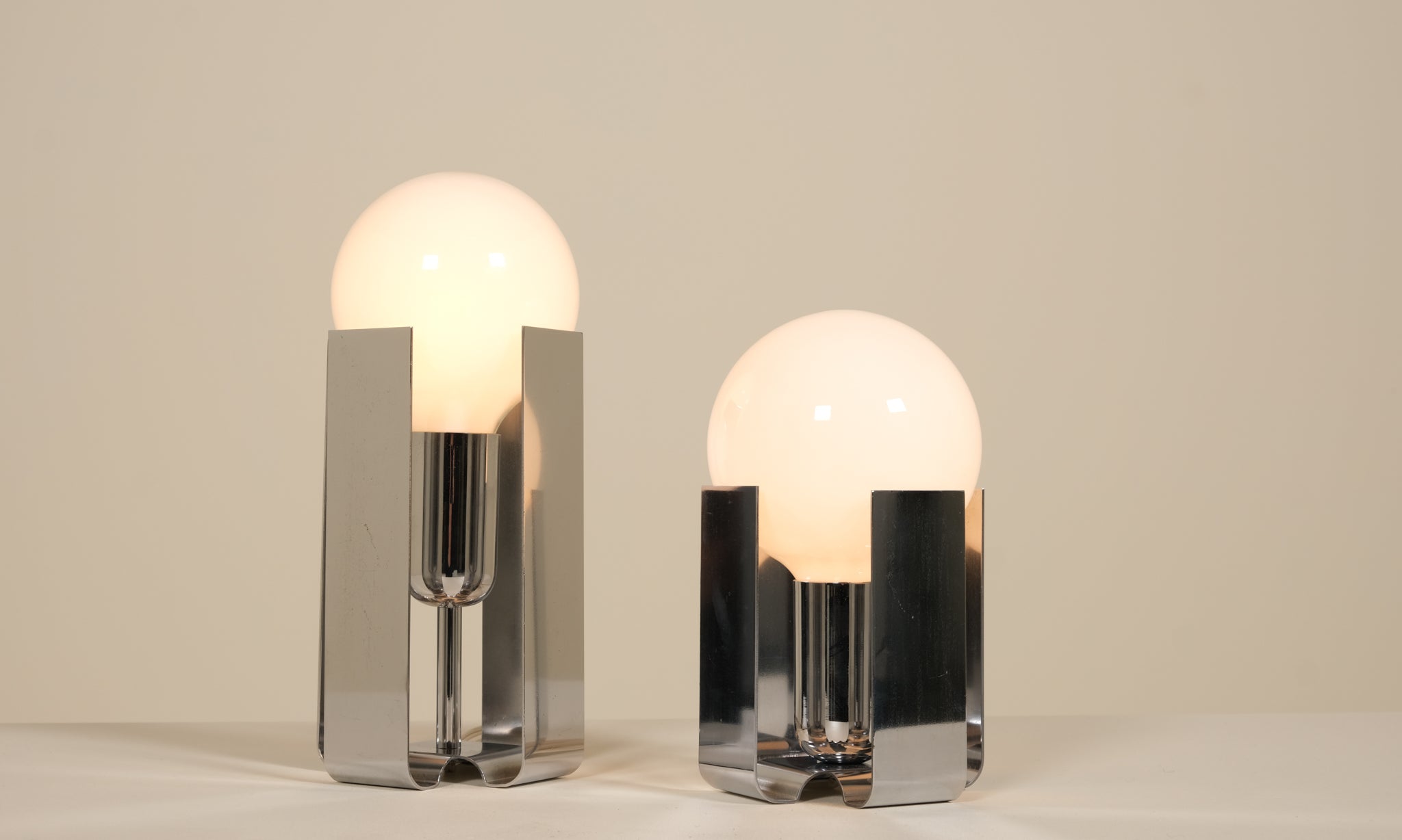 Two modern table lamps with glass shades and chrome bases on a neutral background