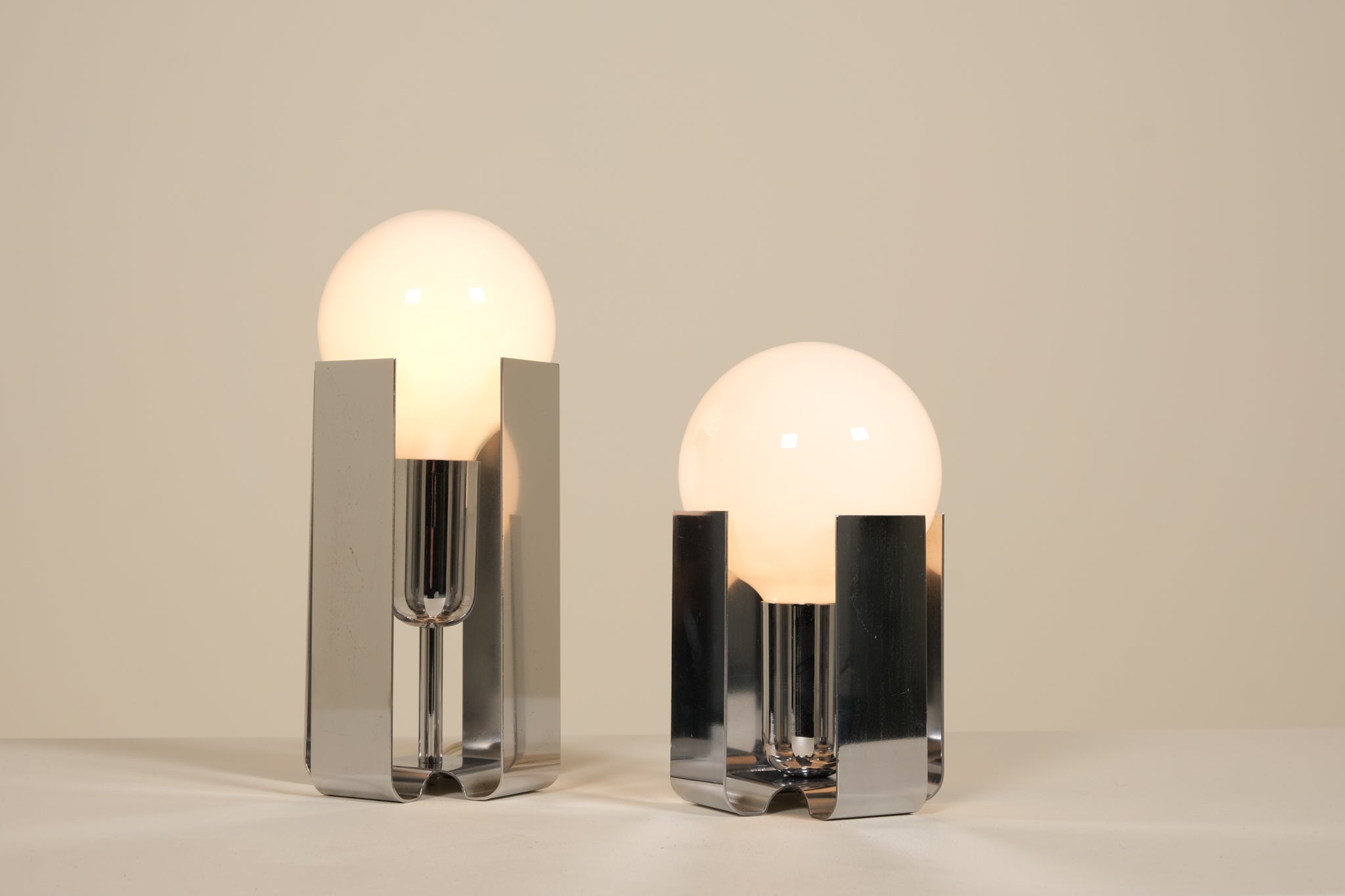 Two modern table lamps with glass shades and chrome bases on a neutral background