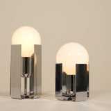 Two modern table lamps with glass shades and chrome bases on a neutral background