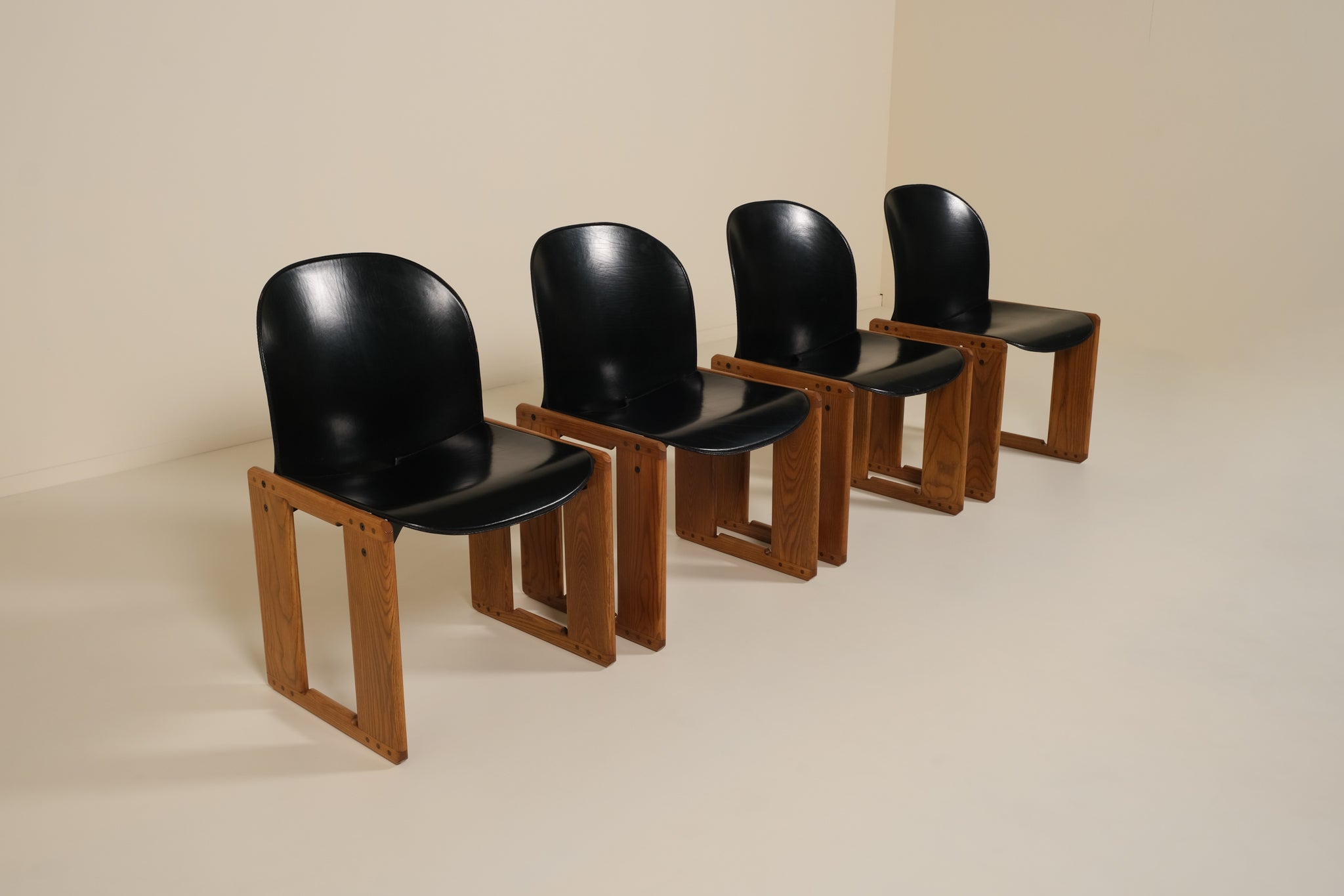 Four black chairs with wooden frames on a beige background