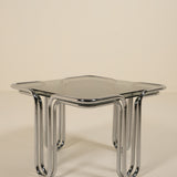 Modern side table with glass top and chrome legs on a beige background