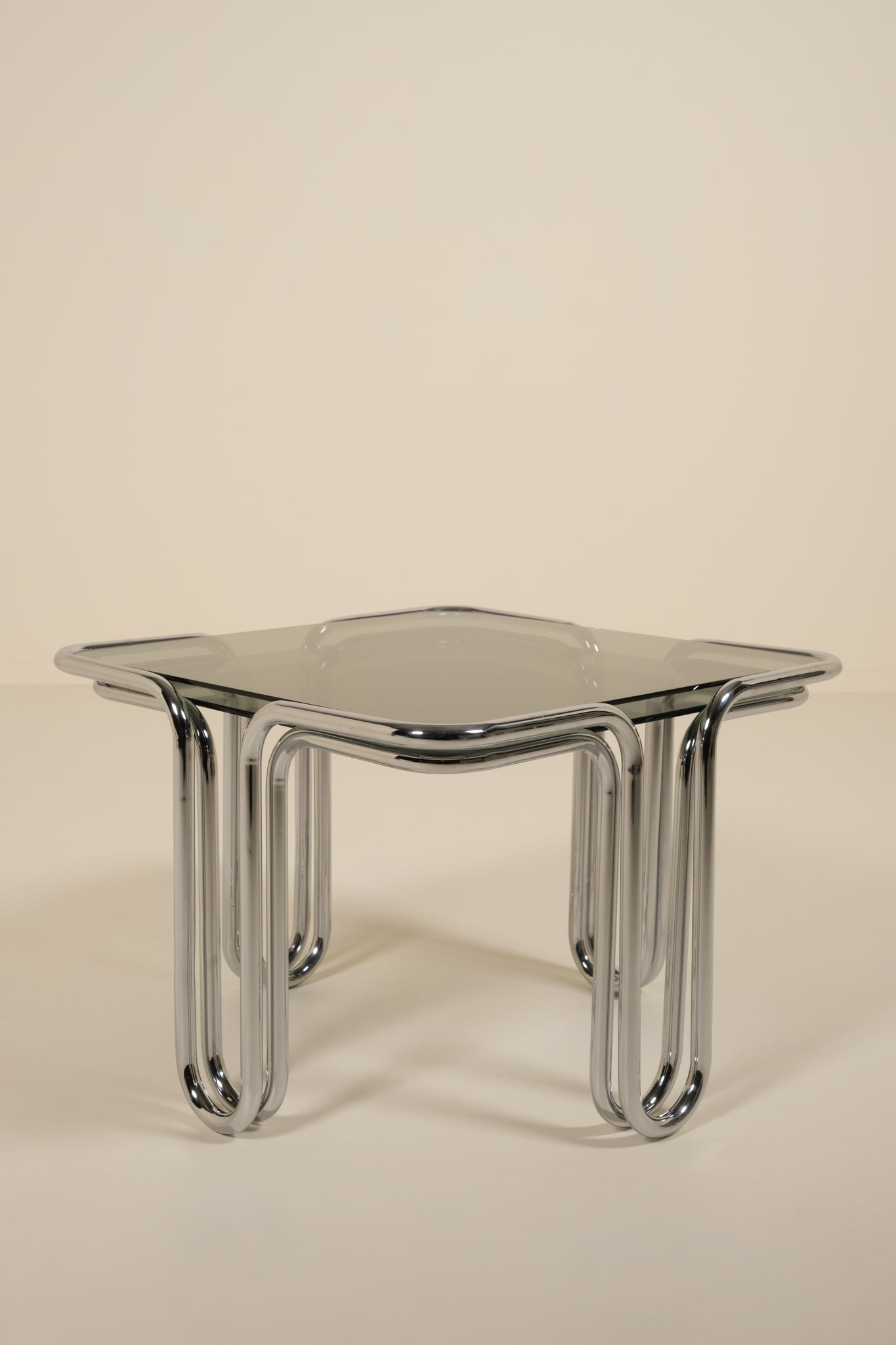 Modern side table with glass top and chrome legs on a beige background