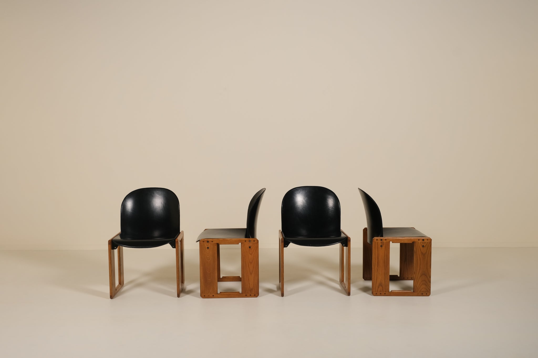 Four black chairs with wooden bases on a beige background