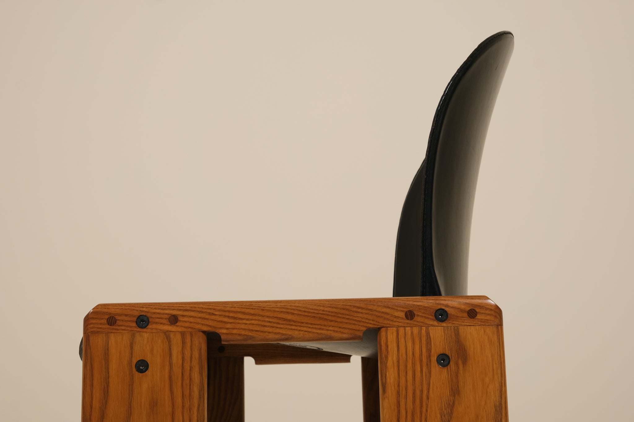 Wooden stool with a black cushioned seat against a beige background