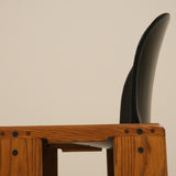 Wooden stool with a black cushioned seat against a beige background