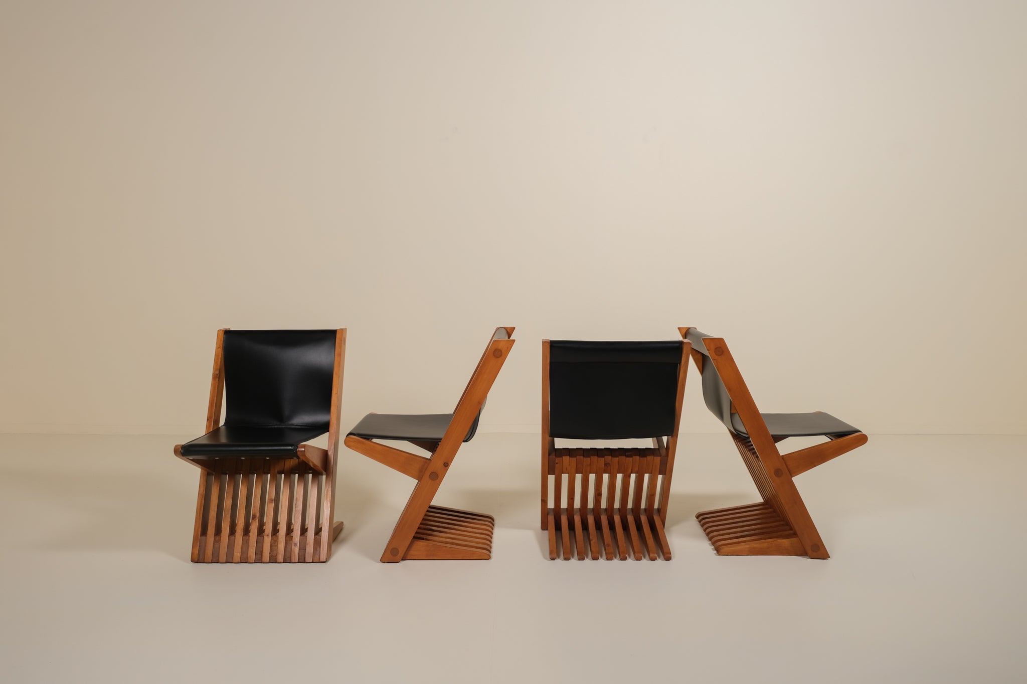 Four modern chairs with black seats and wooden frames on a beige background