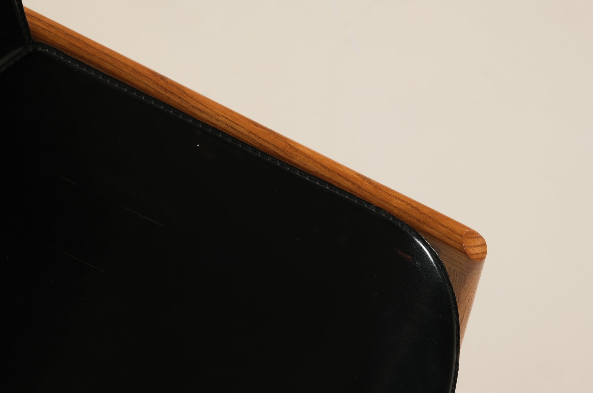 Close-up of a black leather chair with wooden armrest on a beige background