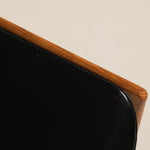 Close-up of a black leather chair with wooden armrest on a beige background