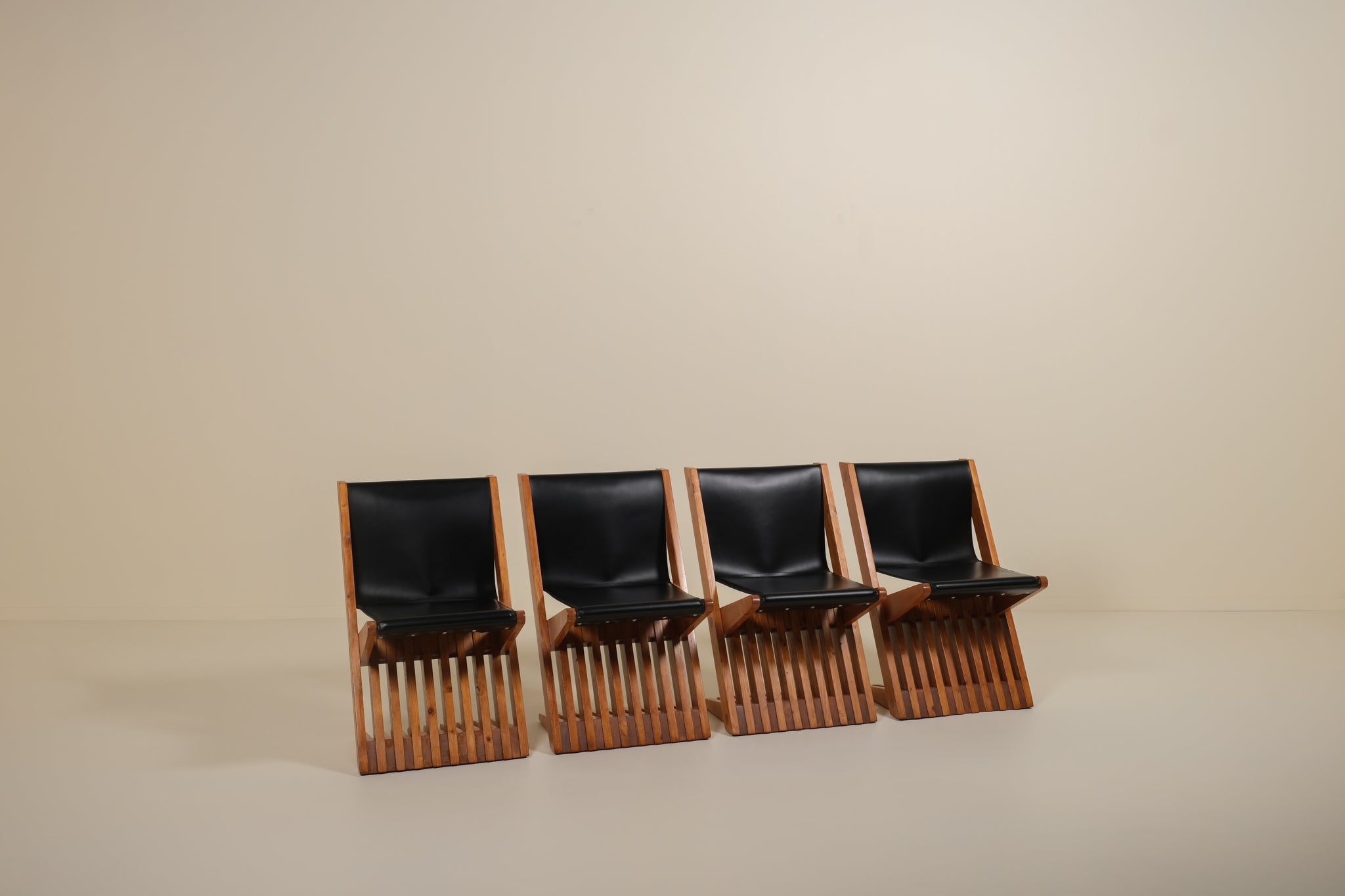 Four black leather chairs with wooden frames arranged in a row on a beige background